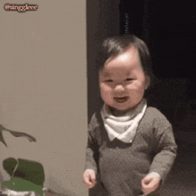 a baby is standing in front of a plant and smiling at the camera .