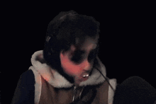 a person is making a funny face in front of a microphone while wearing a hooded jacket and gloves .