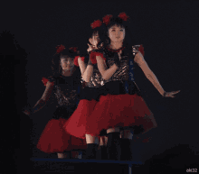 three girls in red and black dresses are dancing on a stage with the number aki32 visible in the lower right corner