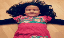 a little girl with curly hair is laying on the floor with her eyes closed
