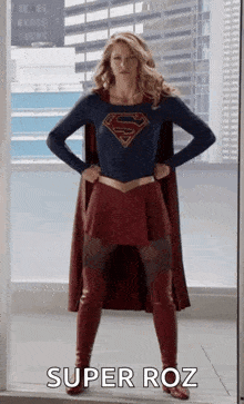 a woman in a superman costume is standing in front of a window with her hands on her hips and says super roz .