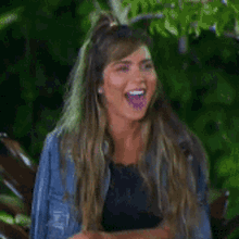 a woman in a denim jacket is laughing and sticking out her tongue .