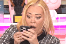 a woman with a surprised look on her face is looking at her phone .
