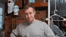 a man in a grey shirt is sitting in front of a brick wall with a hanger on it