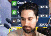a man with a beard is talking into a microphone in front of a screen that says ' drum ' on it .