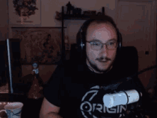 a man wearing headphones and a shirt that says origin stands in front of a microphone