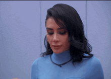 a woman wearing a blue turtleneck sweater looks at the camera