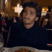 a man is sitting at a table with a plate of food and a glass of wine .