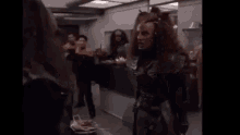 a group of people are standing in a room and a woman is standing in front of them .