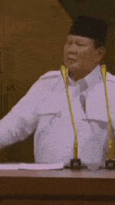 a man in a white shirt is giving a speech in front of two microphones .
