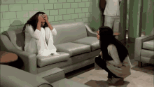 a woman sitting on a couch with her hands on her head talking to another woman