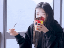 a woman eating a cup of food with chopsticks and a sticker that says ' strawberry ' on it
