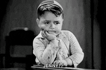 a young boy is sitting at a desk with his hand on his chin and asking jenny .