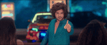 a man with curly hair and a blue shirt is giving a middle finger