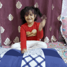 a little girl in a red shirt with a heart on it is sitting on a bed