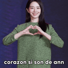 a woman in a green sweater makes a heart with her hands