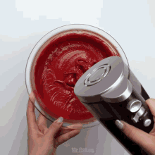 a person is using a mixer in a bowl of red liquid