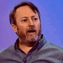 a man with a beard is wearing a blue shirt and a microphone