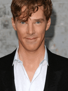 a man with curly hair and blue eyes is wearing a black jacket and a white shirt
