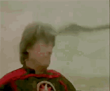 a man with a mustache wearing a red cape and a helmet is looking up at the sky .