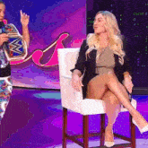 a woman sits in a chair with her legs crossed and a man stands behind her