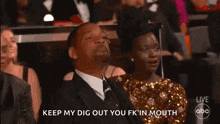 a man in a suit and tie is sitting in a theatre with a woman in a gold dress behind him .