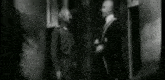 a black and white photo of two men talking to each other .