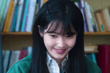 a woman with long black hair and bangs is smiling in front of a bookshelf