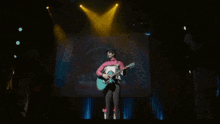 a man is playing a guitar on a stage in front of a screen that says ' x ' on it