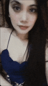 a woman with long dark hair is wearing a blue top and a necklace