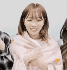 a girl is wrapped in a pink blanket and smiling while standing next to another girl .