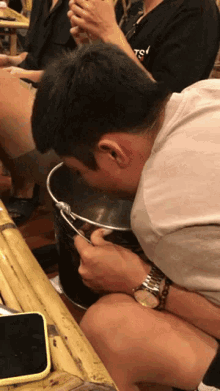 a man wearing a watch and a t-shirt that says ts is drinking from a bucket