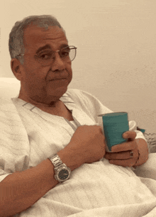 a man in a hospital gown is holding a cup and wearing a silver watch
