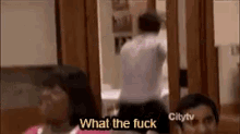 a man is standing in front of a woman in a room and says `` what the fuck '' while a woman looks on .