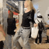 a woman in a black shirt and blue jeans is walking in a crowded area .