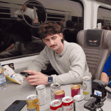 a man sits at a table surrounded by cans including a can of absolut