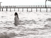 a woman in a white dress is standing in the water near a pier .