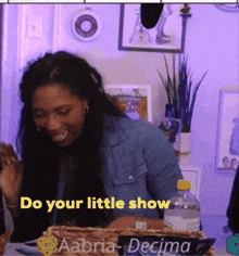 a woman sitting at a table with a sign that says do your little show on it