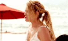a woman in a white dress is standing on a beach with a red umbrella .