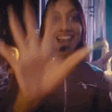 a woman is smiling and waving her hand in front of a crowd .