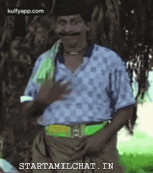 a man with a mustache is standing in front of a tree holding his hand to his chest .