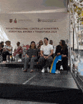 a group of people sit on a stage in front of a sign that says dia internacional contra la homofobia