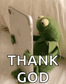 kermit the frog is sitting in front of a cell phone and saying `` thank god '' .
