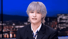 a young man with gray hair and a suit and tie looks at the camera