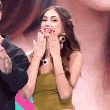 a woman in a green top is covering her mouth with her hands while a man stands behind her .