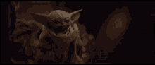 a baby yoda is sitting in a dark room with a scarf around its neck .