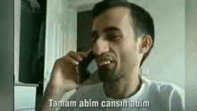 a man in a white shirt is talking on a cell phone and smiling .