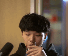 a young man is drinking from a glass in front of two microphones