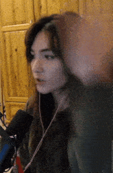 a woman wearing headphones and a green shirt stands in front of a microphone and a wooden cabinet