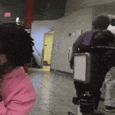 a person wearing a pink hoodie is standing in a hallway with a camera